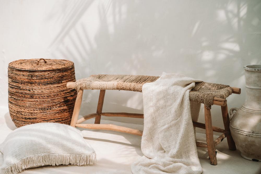 Een geweldige lounge indeling met een raffia bankje, katoenen kussens en een prachtige mand. Ideaal voor een coastal living vibe bij Casa Calida